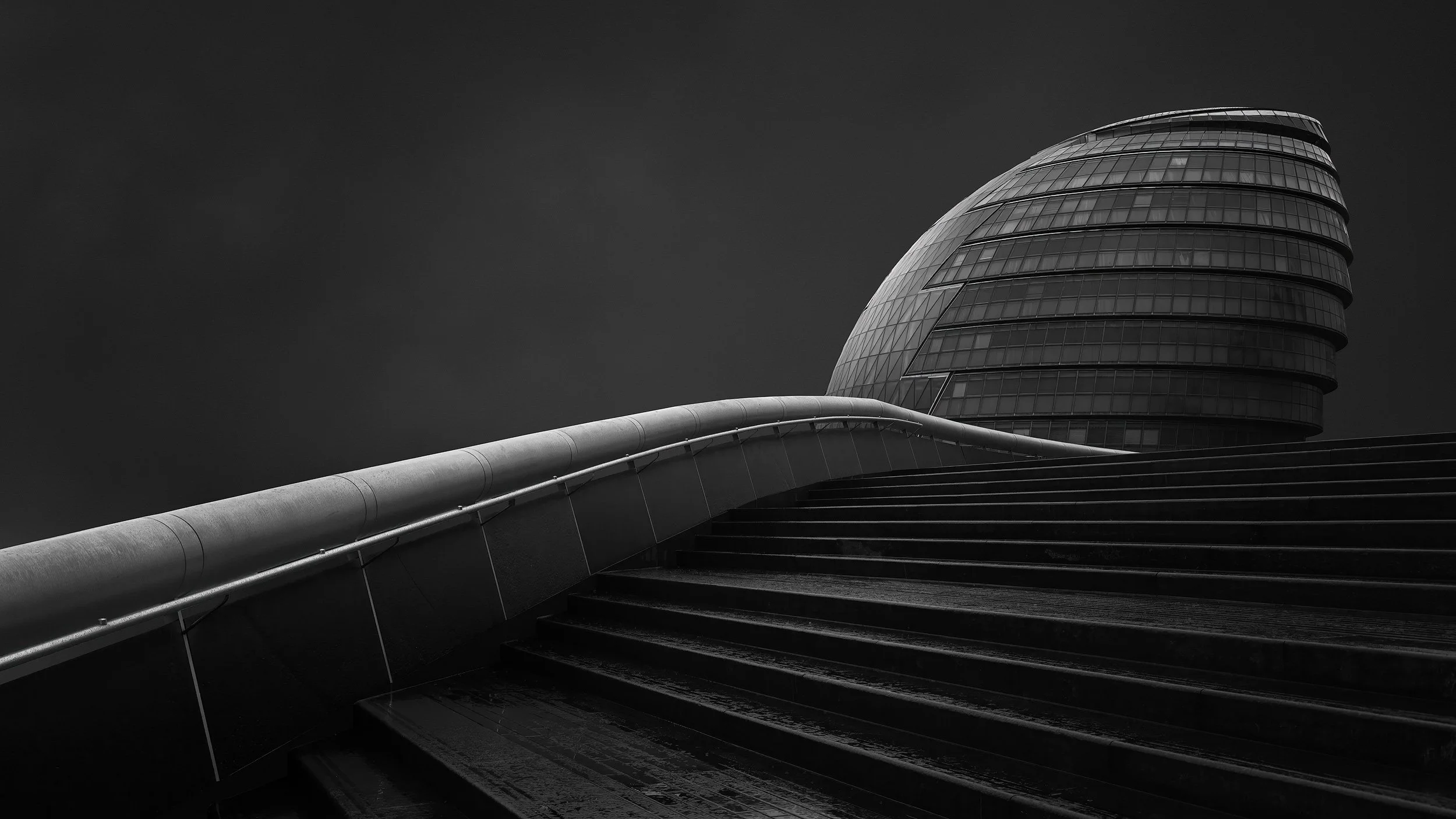 Contemporary civic architecture in Southwark, London: A dramatic monochromatic study of the former London City Hall, designed by Foster + Partners. This architectural photograph captures the building’s iconic bulbous form and glass-banded facade from