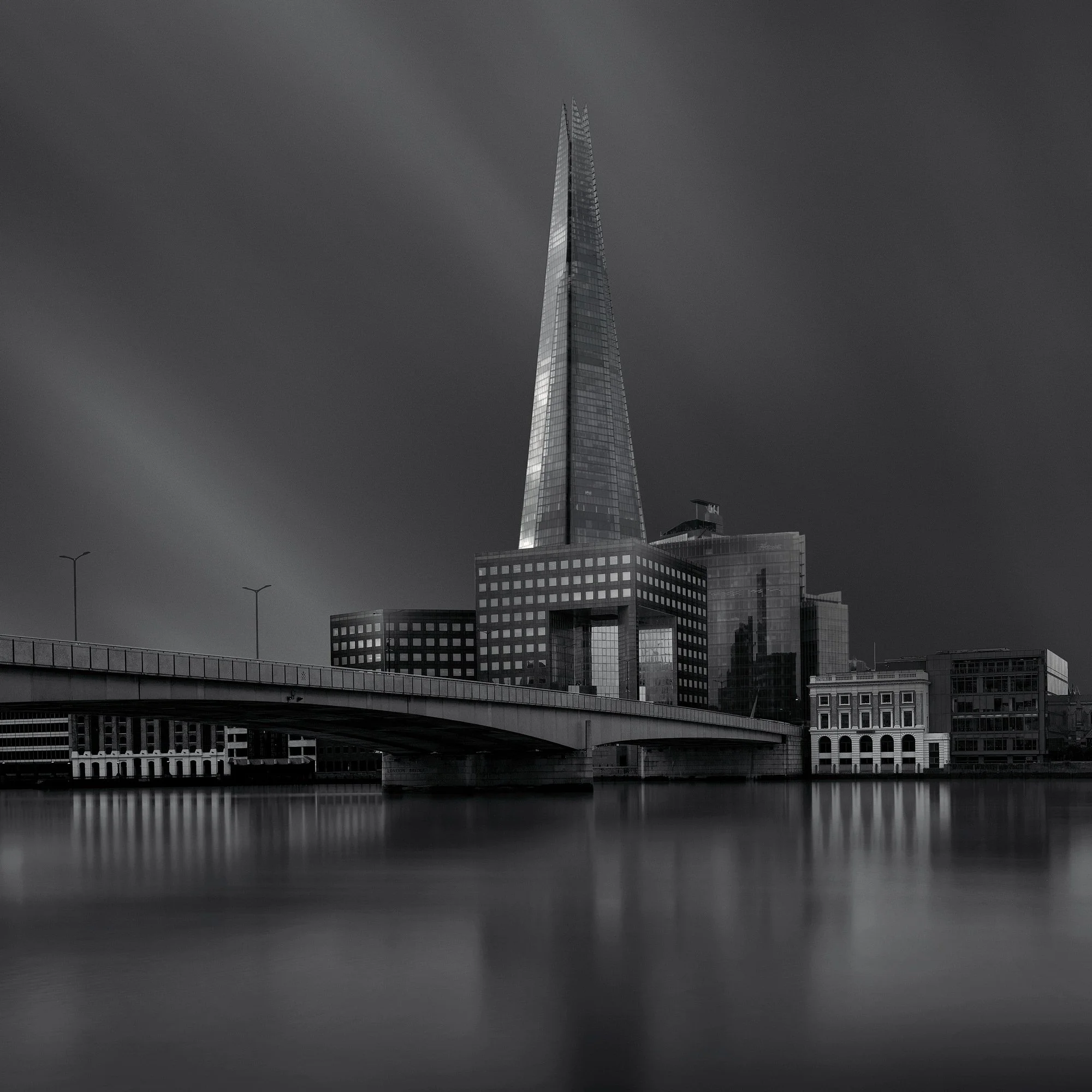 [architecture] [uk] [london] [blackandwhite] [square] The Shard B&W long exposure from London Bridge, sharp glass spire rising behind the arch and Southwark skyline. Architectural Photography by Jim Scott.