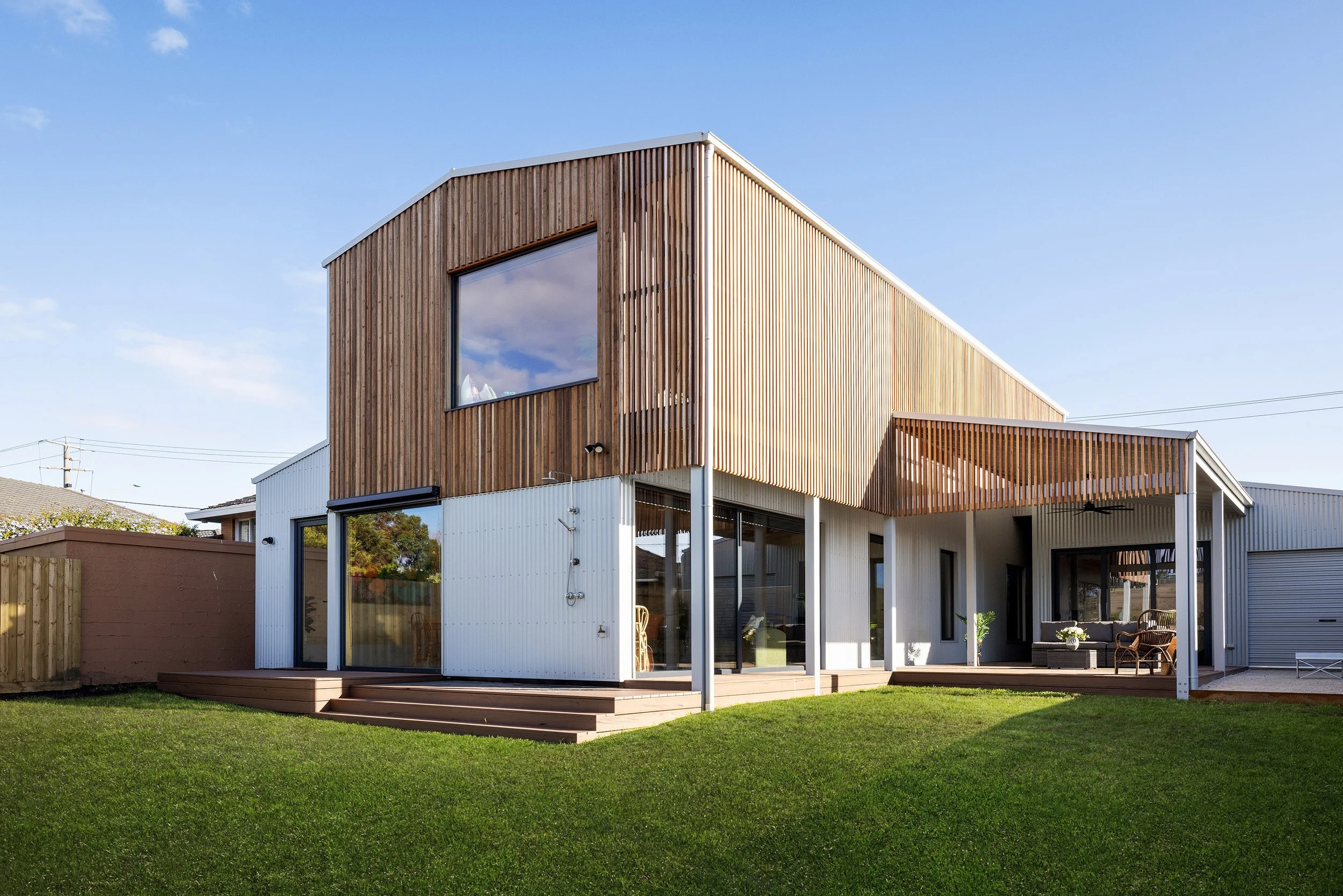 Modern two-story coastal home featuring a timber upper level and white lower level with large glass sliding doors. A prime example of contemporary architecture designed for the Great Ocean Road, Port Fairy, and Warrnambool region.
