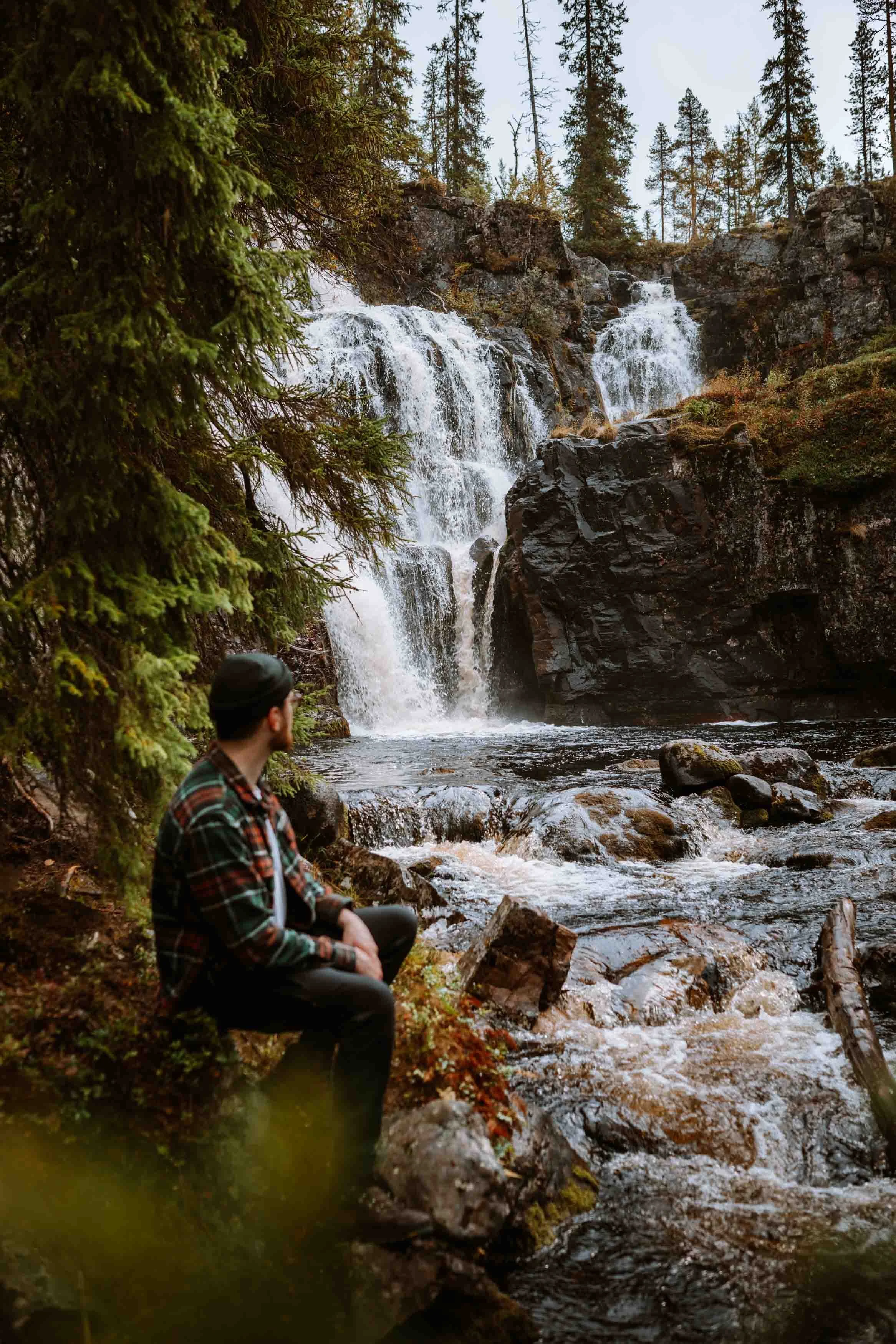 Man sitting in forest at the foot of a waterfall