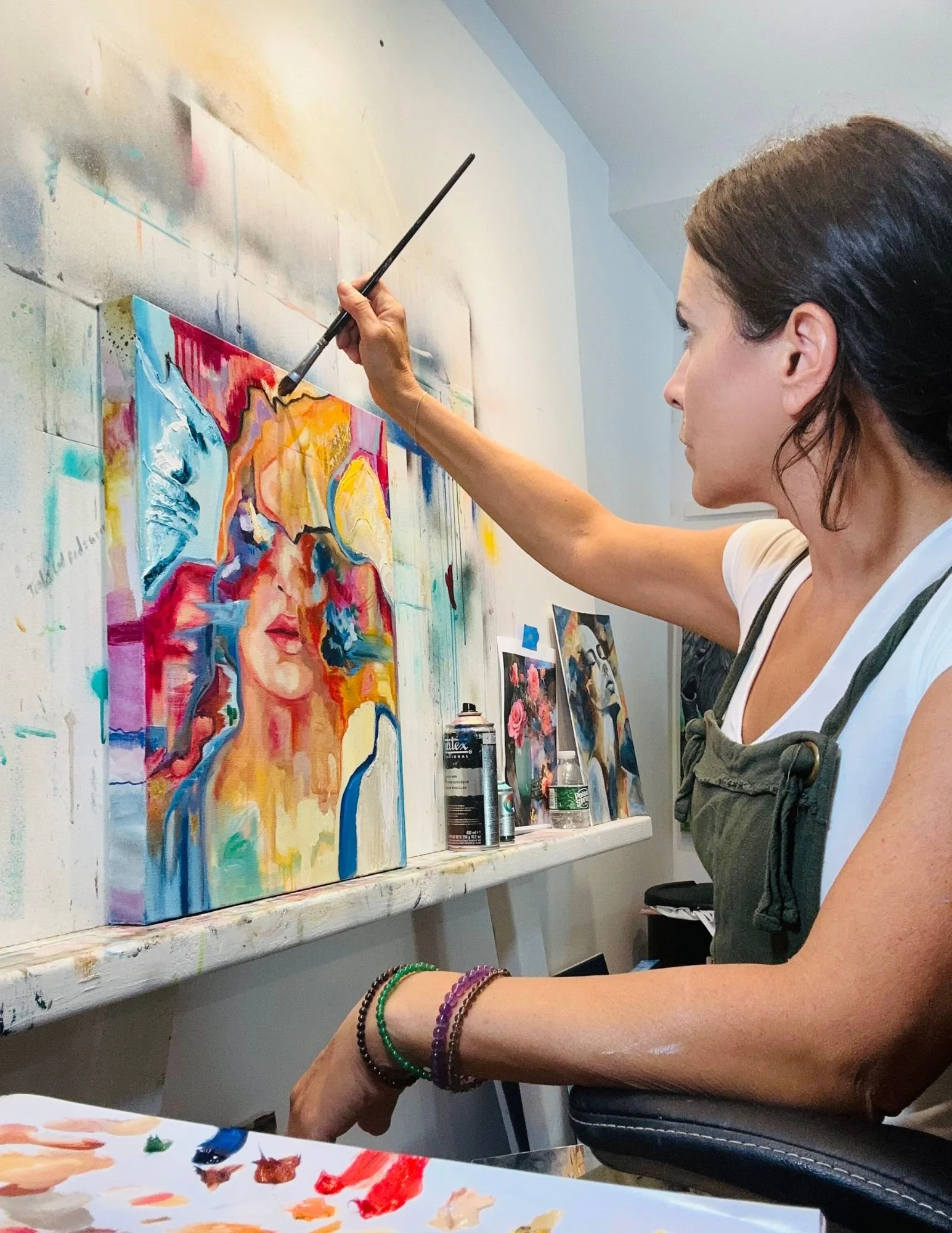 Tracey painting a colorful abstract portrait on a canvas in an art studio.
