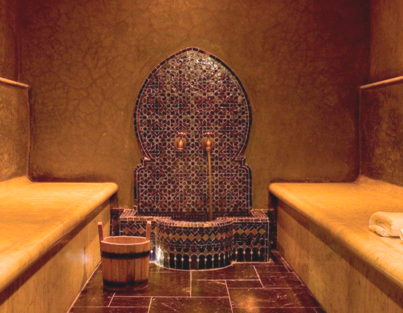Person practicing yoga in an indoor studio with stone walls, wooden ceiling beams, and a door opening to sunlight.