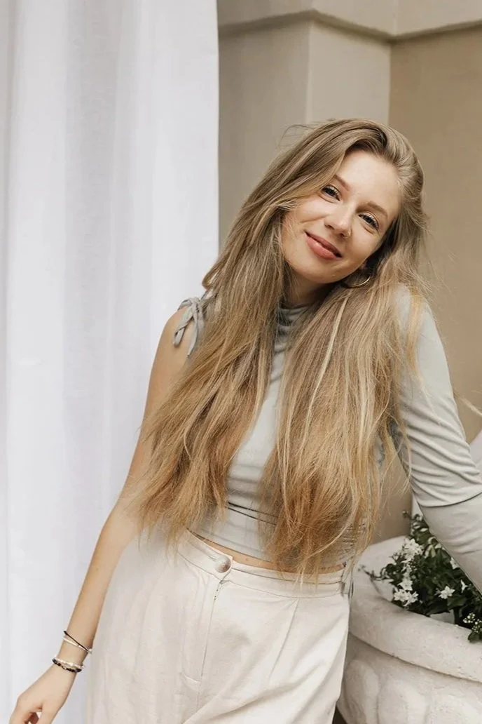 frau-mit-langen-blonden-haaren-in-hellem-outfit-an-steinernem-brunnen