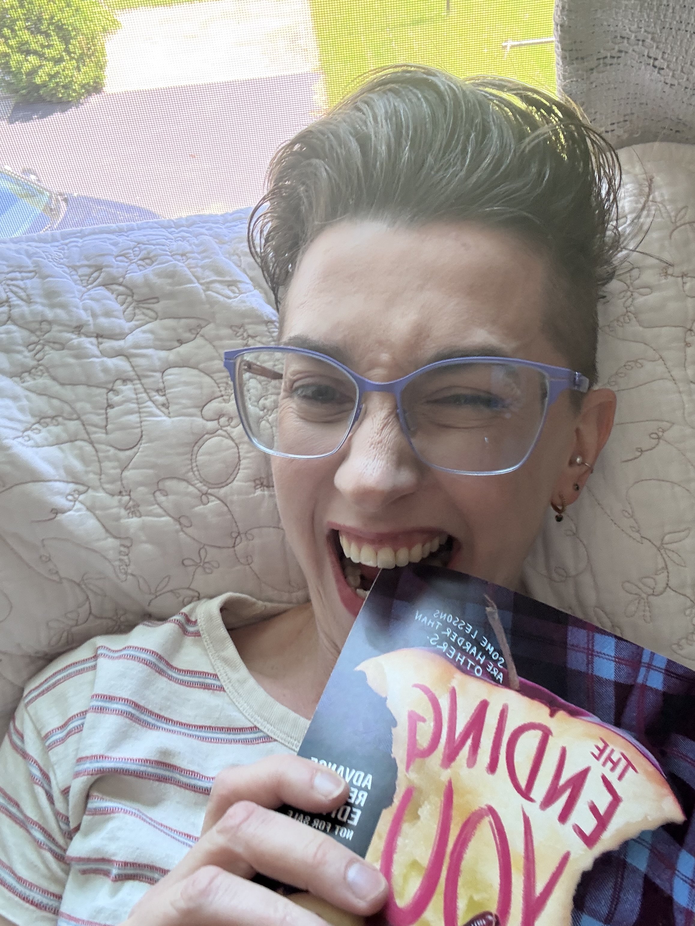 the author rebecca stafford is biting an advance reader copy of her book, the ending you deserve