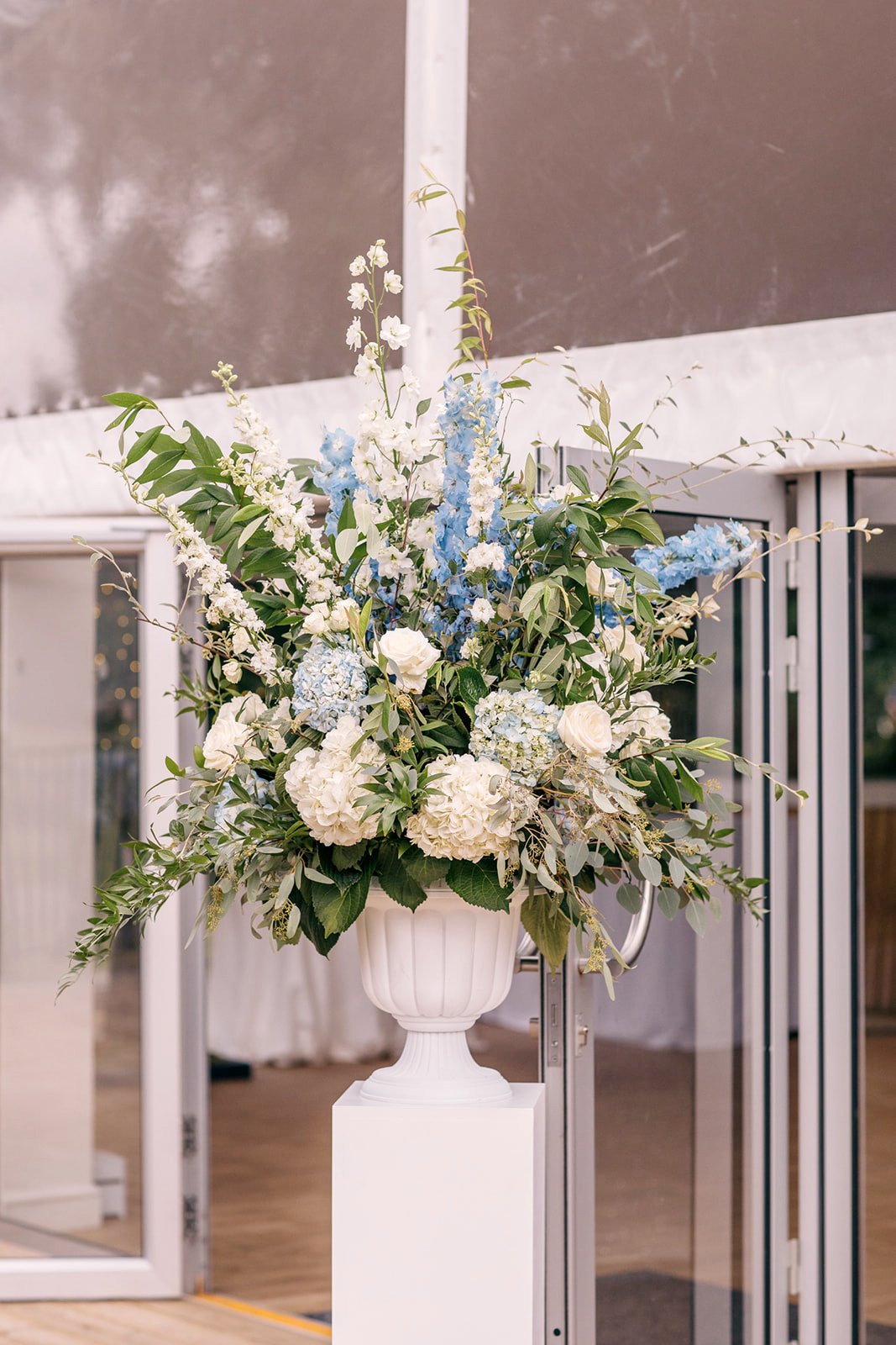 Large white and blue floral urn arrangement on a pedestal at the entrance to the wedding reception marquee at Chiswick House & Gardens.