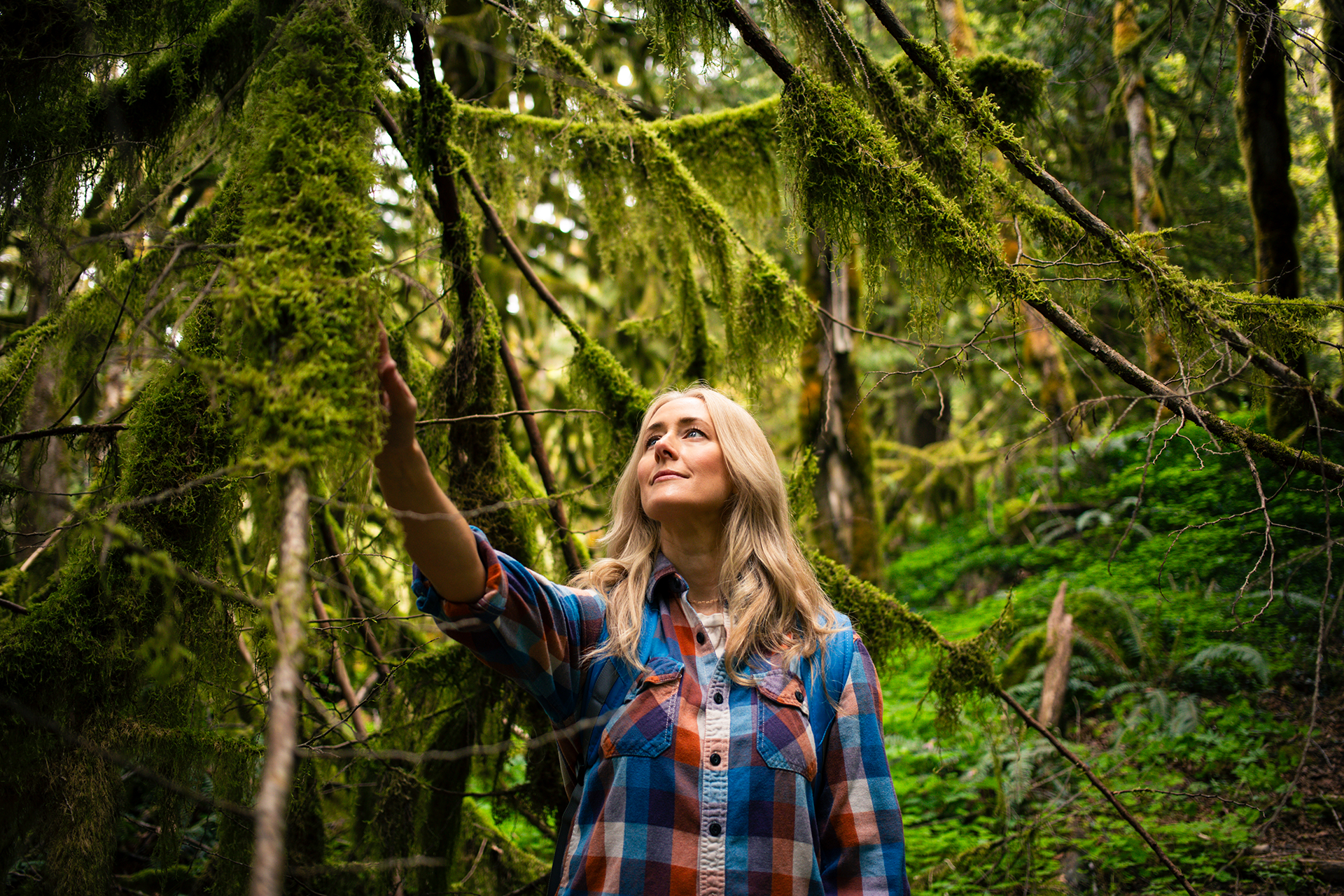 Blonde woman in a plaid shirt exploring a moss-covered forest