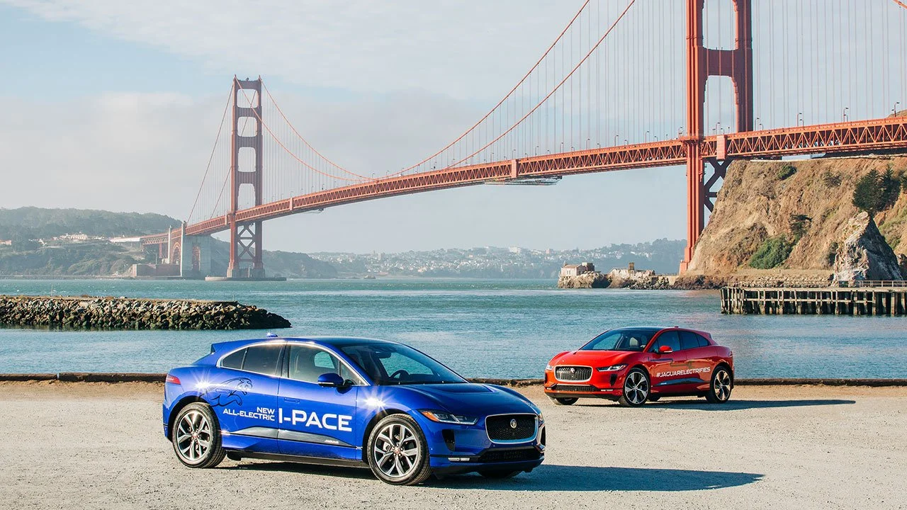 Blue Jaguar I-PACE electric SUV and red Jaguar electric vehicle parked beneath the Golden Gate Bridge in San Francisco