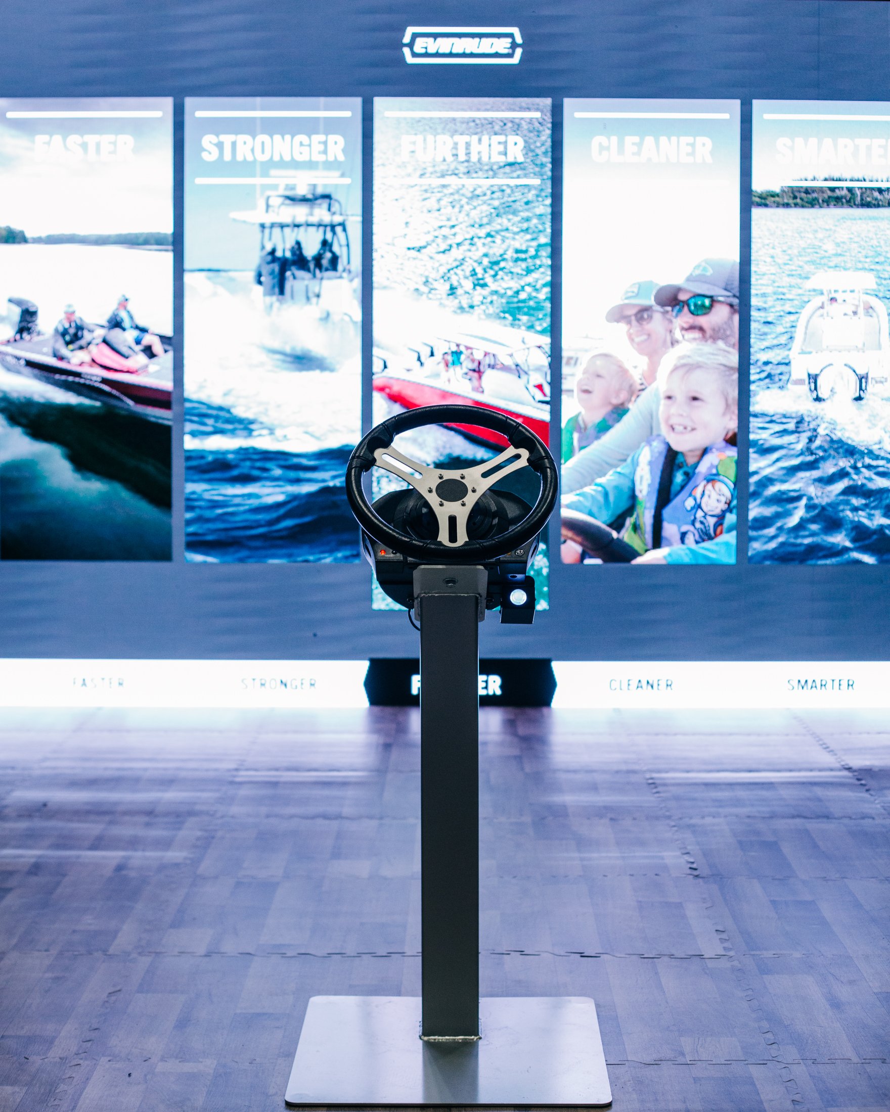 Evinrude boat simulator display with steering wheel and panels labeled Faster, Stronger, Further, Cleaner, and Smarter