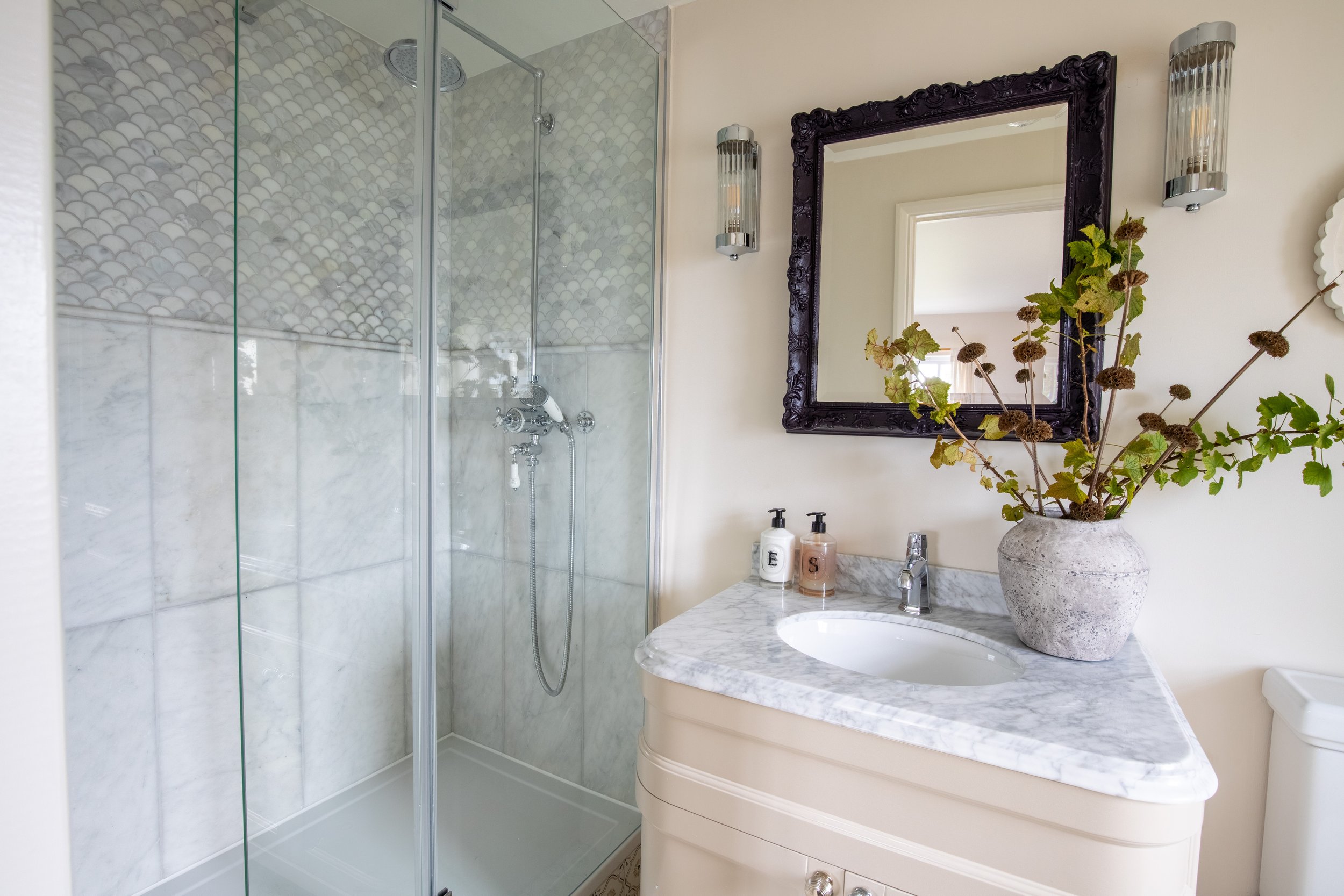 Modern wooden house with large glass window set against mountainous landscape with yellowish grass and small trees in the foreground.