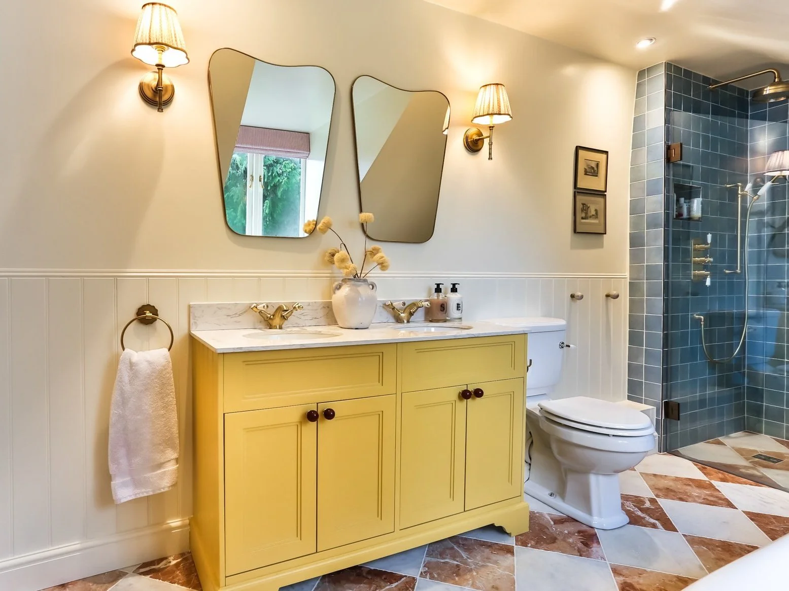 Bathroom with yellow vanity, two mirrors, wall-mounted lamps, and a walk-in shower with blue tiles.