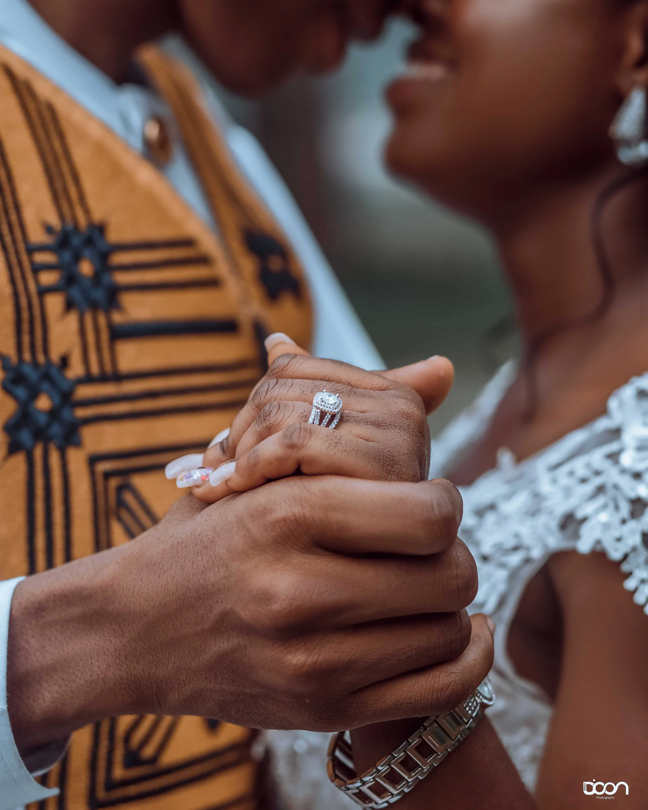 Close-up of a couple holding hands, with focus on the bride's engagement ring and wedding band, during a wedding ceremony.