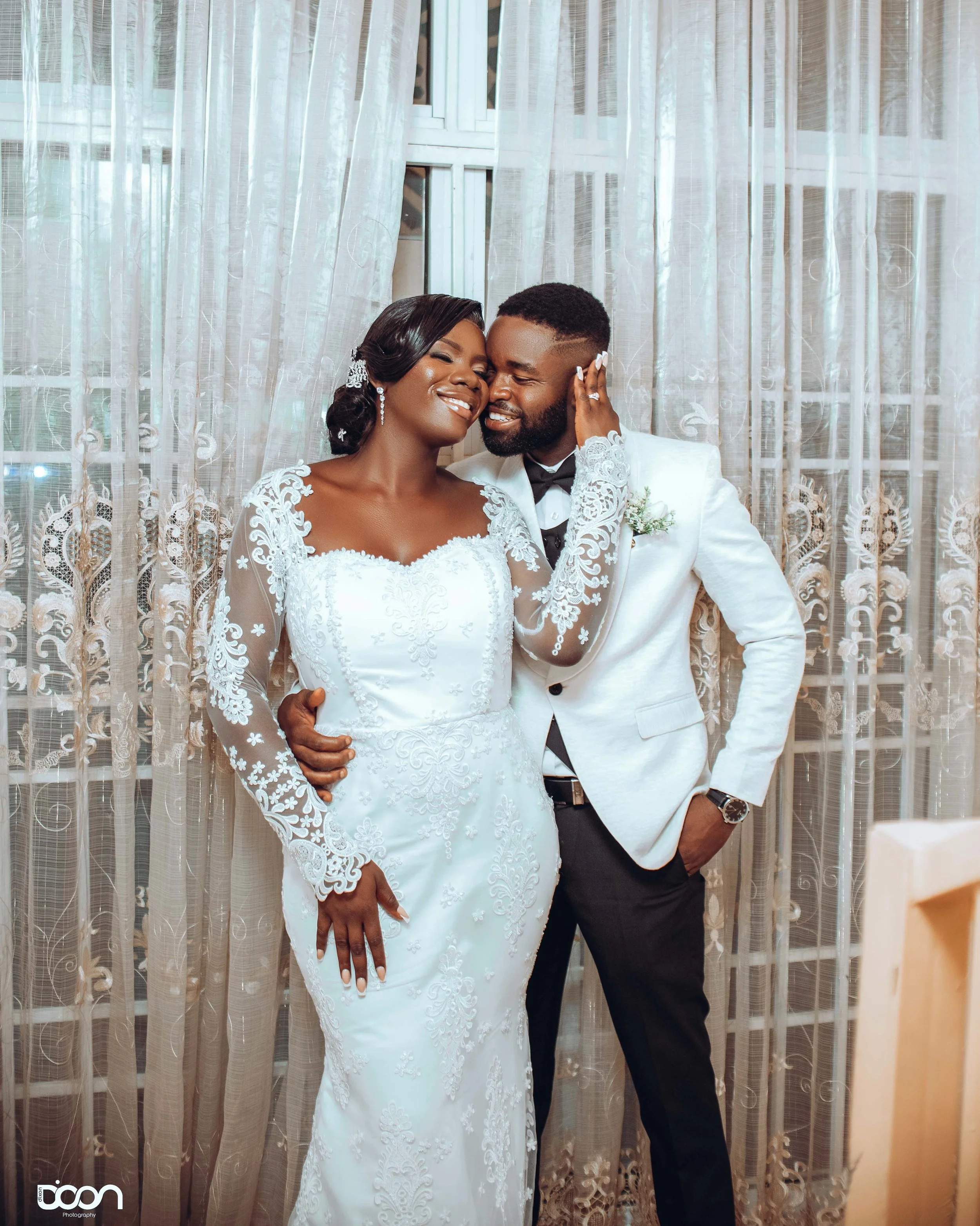 A bride and groom celebrating their wedding, smiling and holding each other against a curtain backdrop.