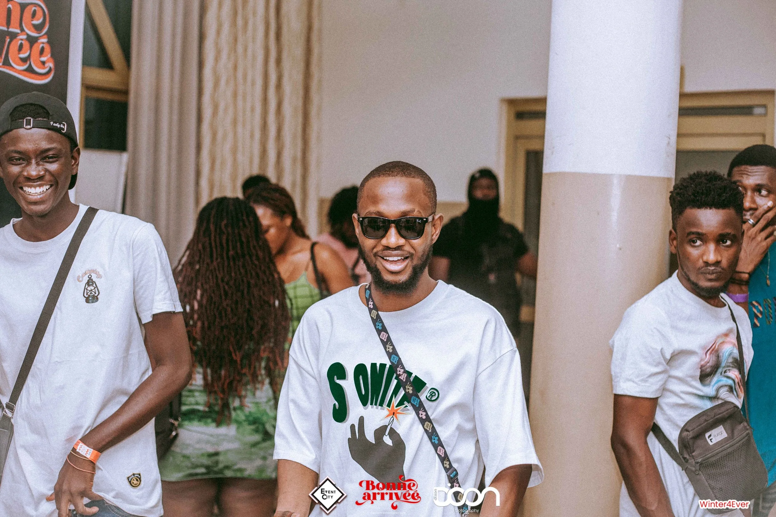 Group of young men smiling and posing at an indoor event, with some wearing sunglasses and casual clothing.