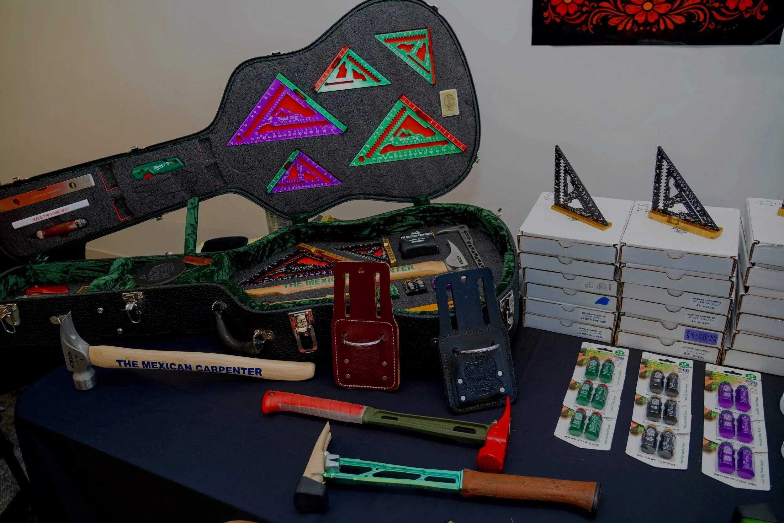 A display of various colorful carpenter measuring tools, squares, and hammers arranged on a table, with some tools inside and outside a large black carrying case.