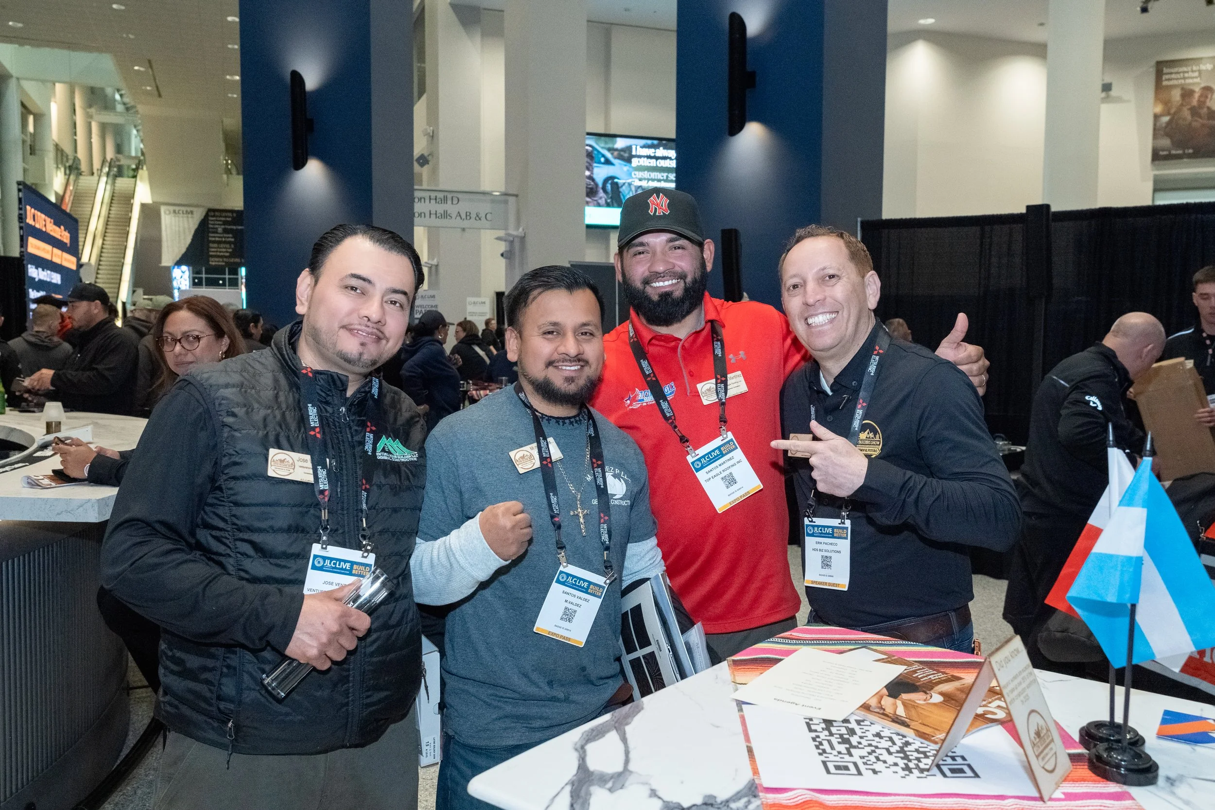 Four men standing together at a conference, smiling and posing for the camera, with a busy conference hall in the background.