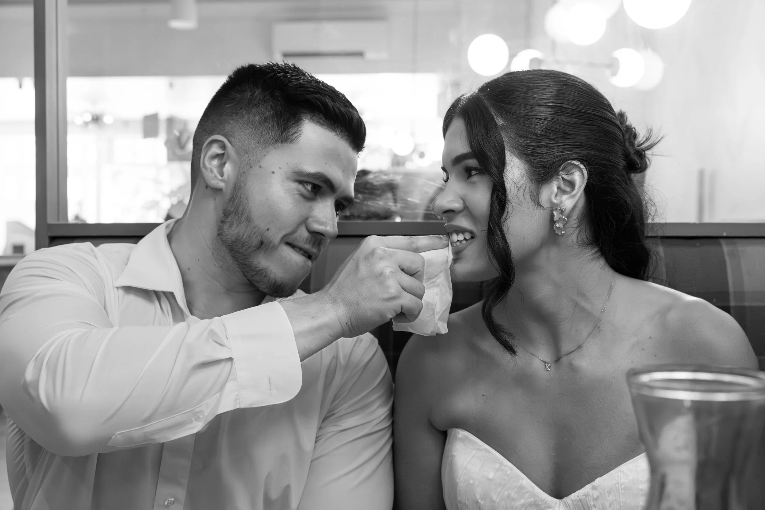 A young man feeds a young woman in a restaurant, both smiling and making eye contact.