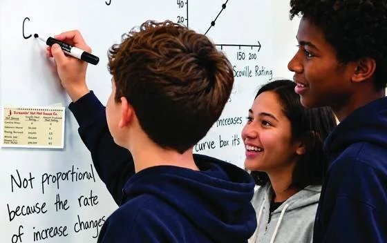 Three students discuss mathematics at a whiteboard.