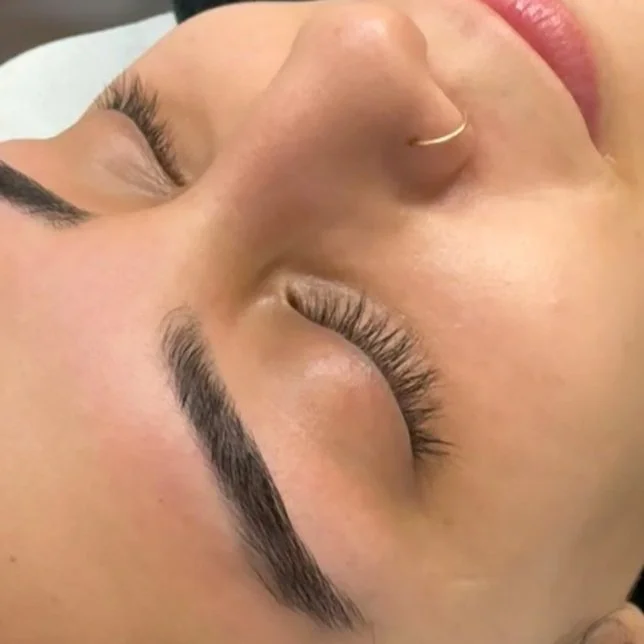Close-up of a woman's face, showing her forehead, closed eyes with long eyelashes, a small nose with a nose ring, and closed lips.