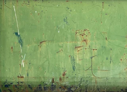 A close-up view of a textured green surface with visible scratches, faded marks, and subtle hints of rust, creating a distressed, abstract look with earthy undertones.