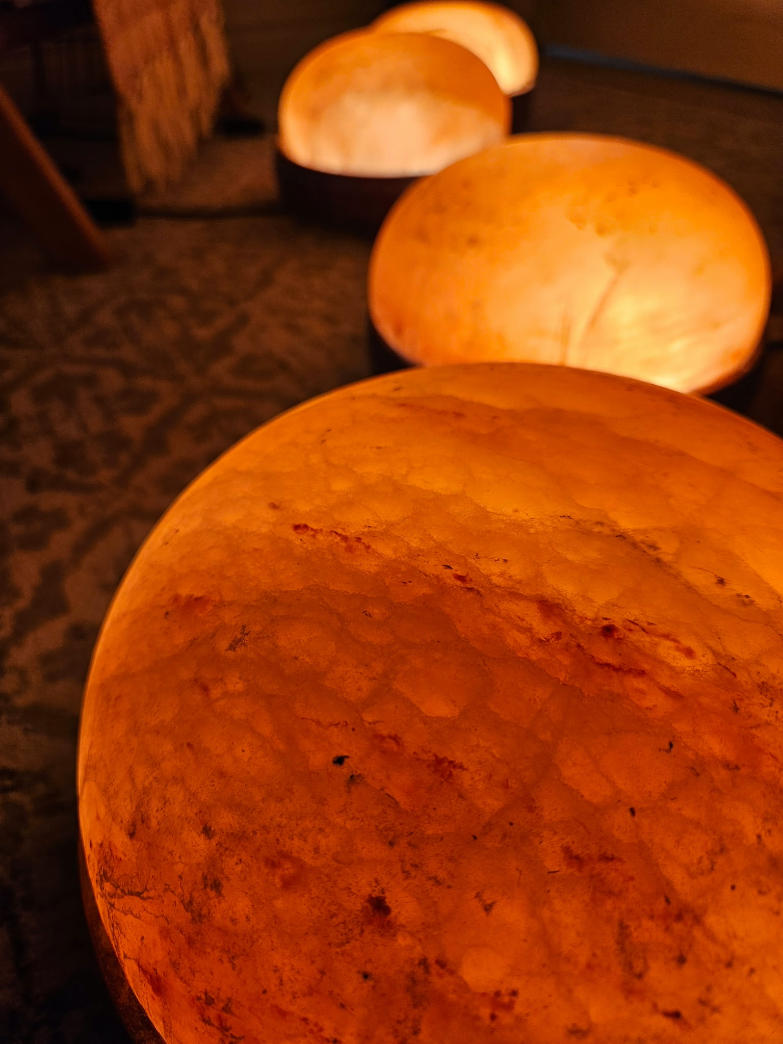 Close-up of orange Himalayan salt lamps with a rough surface and warm glow in a dimly lit room.