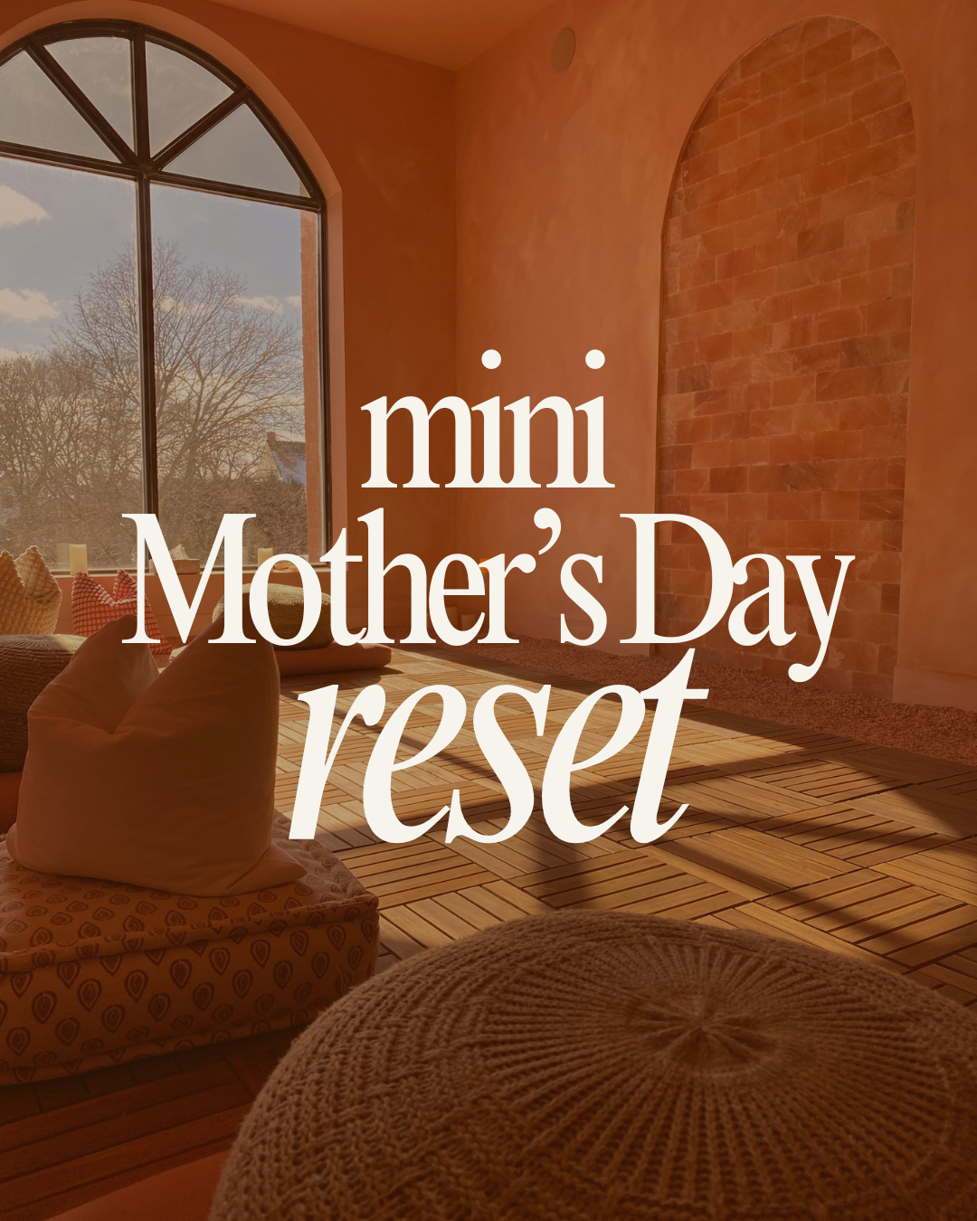 A cozy room with large arched window letting in natural light, featuring a brick wall, wooden floor, and soft cushions on the floor. Overlaid text reads 'mini Mother’s Day reset.'