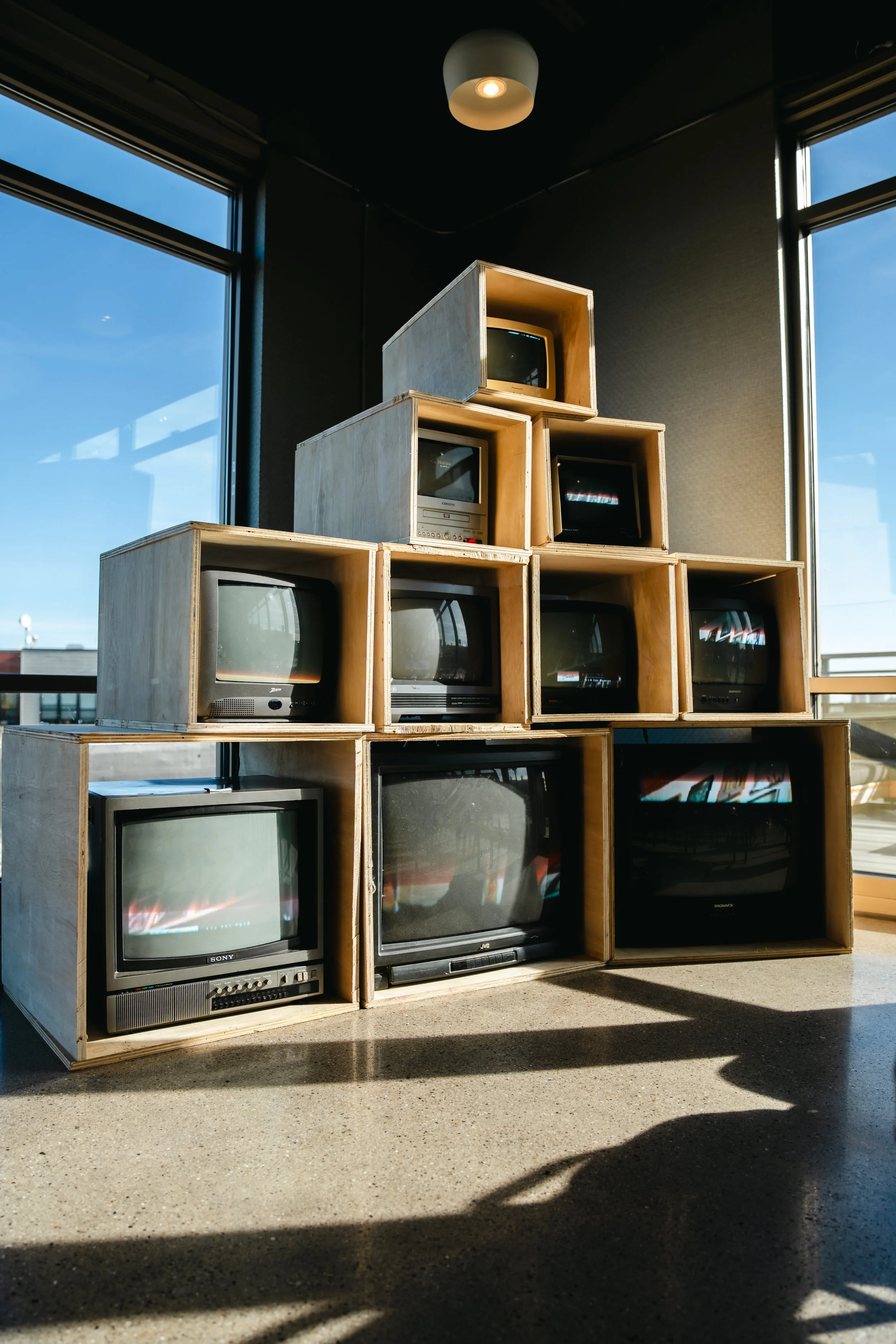 Stacked wooden crates filled with vintage televisions inside a room with large windows and natural light.