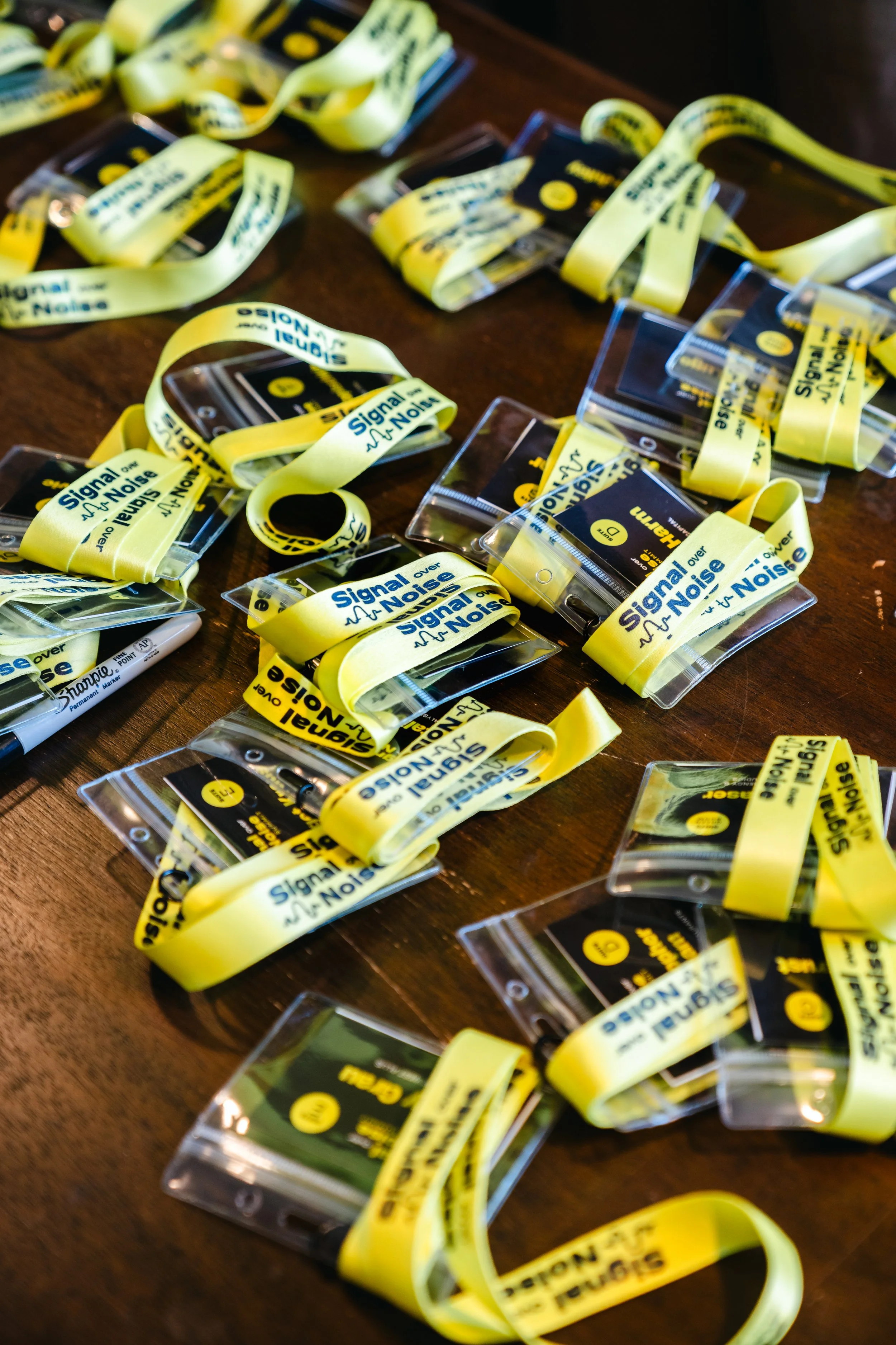 Close-up of several yellow wristbands with black text reading 'Signal over Noise' and a graphic of a heartbeat line, placed on a wooden surface.