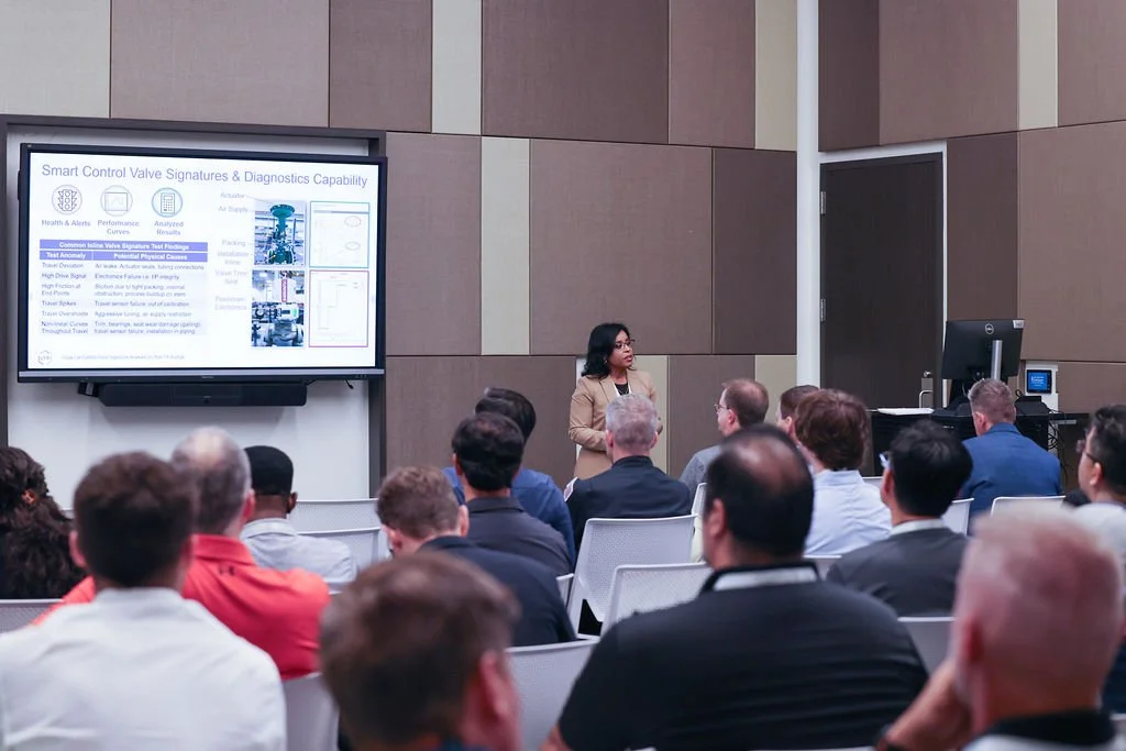 A woman presenter giving a talk on smart control valve signatures and diagnostics to an audience in a conference room.