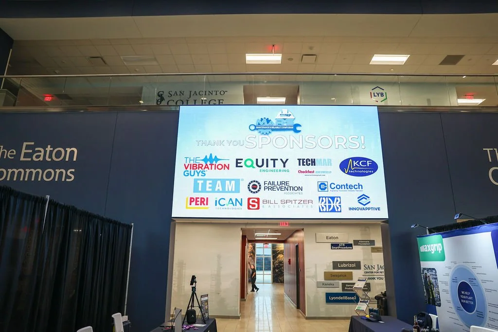 Large digital screen displaying sponsor logos and thank you message at an indoor event, with doorway leading to another room in the background.