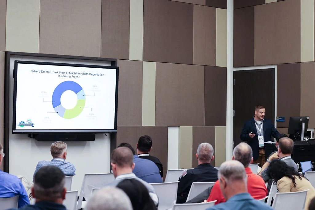 A man presenting in front of an audience during a conference or seminar, with a large screen displaying a chart titled 'Where Do You Think Most Machine Health Degradation is Coming From?'