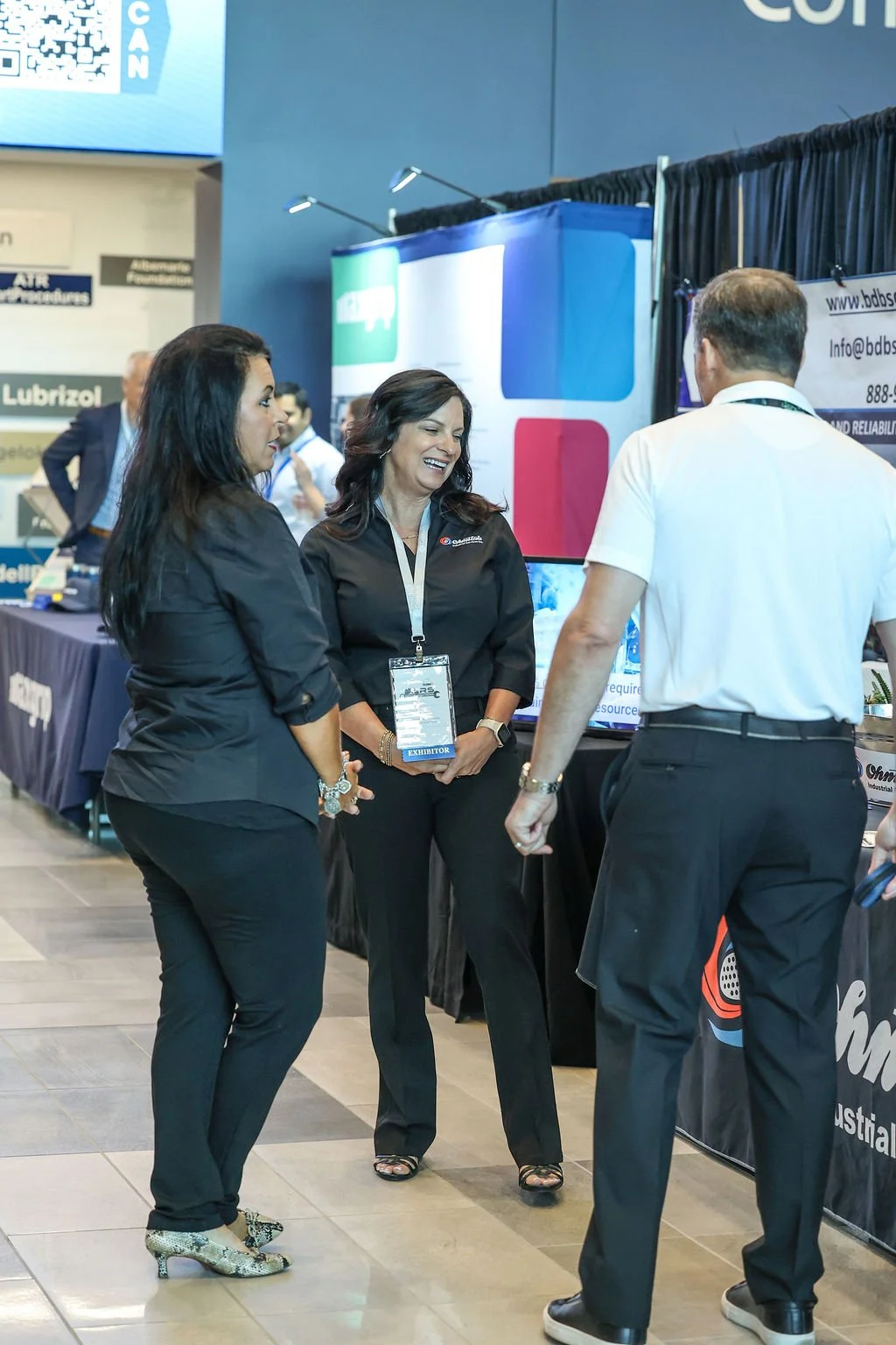 Three businesspeople, two women and one man, are having a conversation at a trade show or conference.
