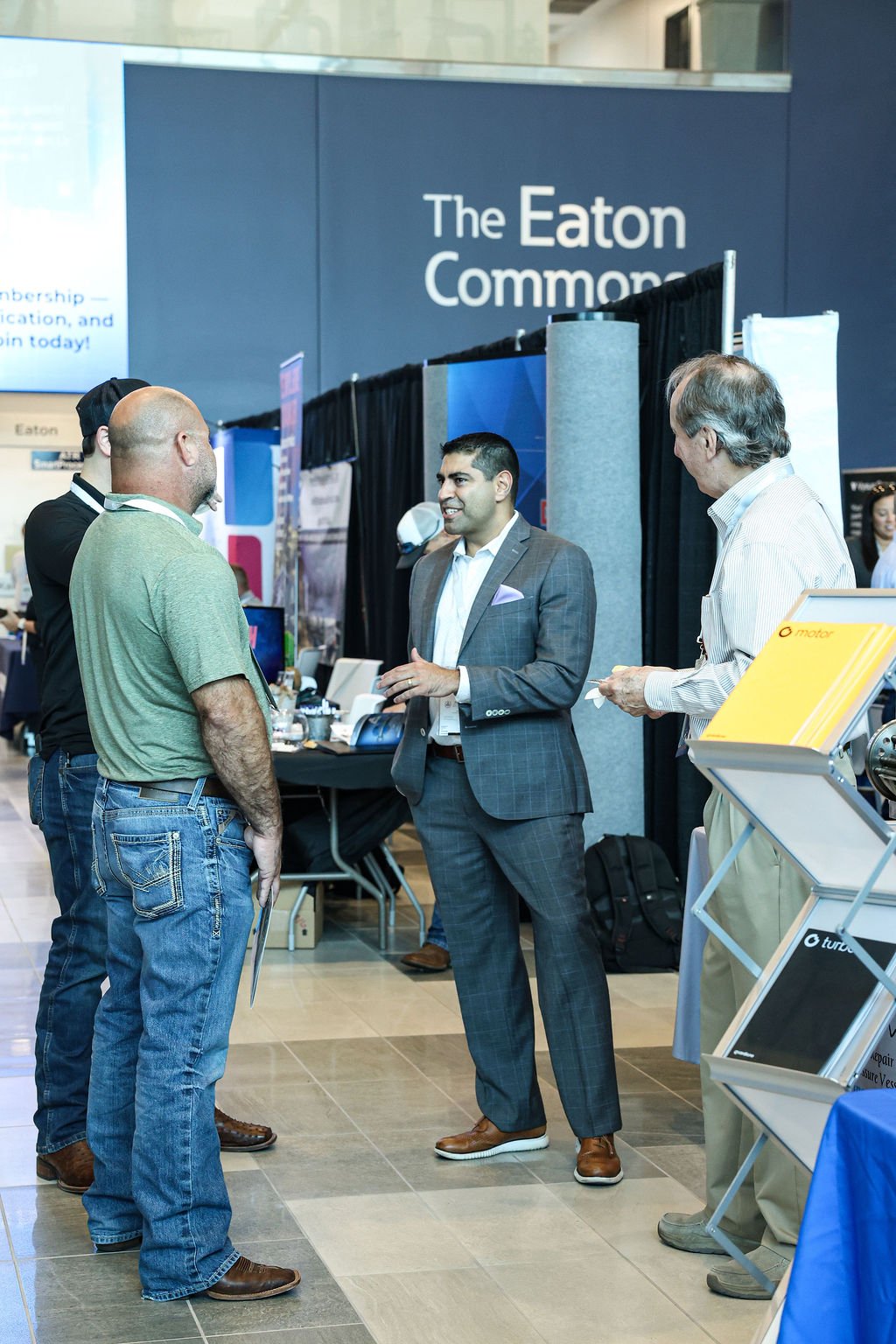 People having a conversation at an exhibition booth with a sign that reads 'The Eaton Commerce'