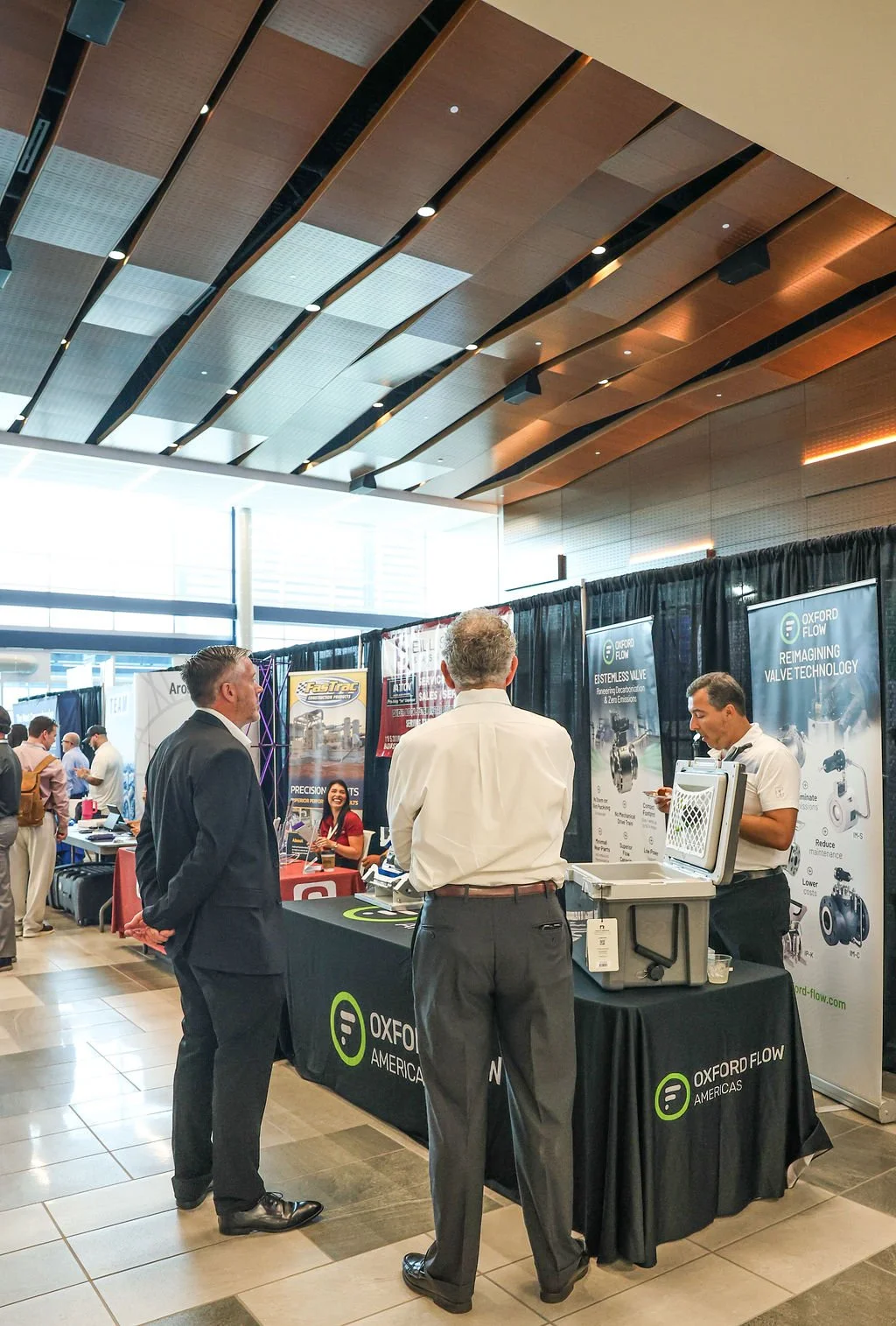 Business professionals at a trade show booth for Oxford Flow Americas, displaying valve technology and engaging in discussion.