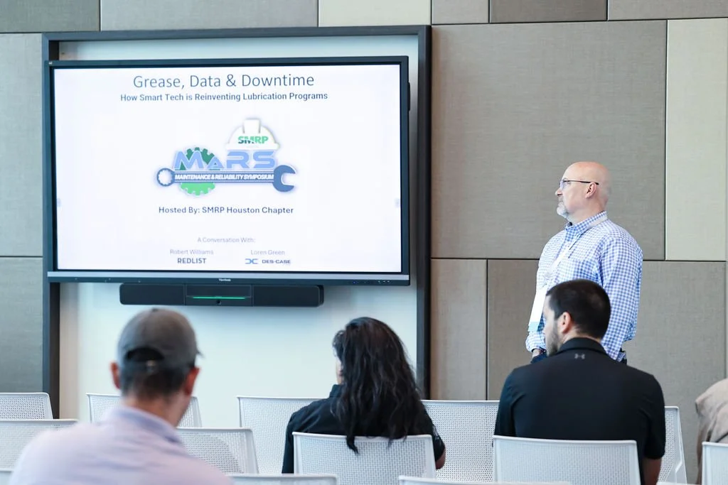 A presentation slide titled 'Grease, Data & Downtime: How Smart Tech is Reinventing Lubrication Programs,' displayed on a large screen at a conference. The slide shows the event is hosted by SMRP Houston Chapter with speakers Robert Williams and Lore