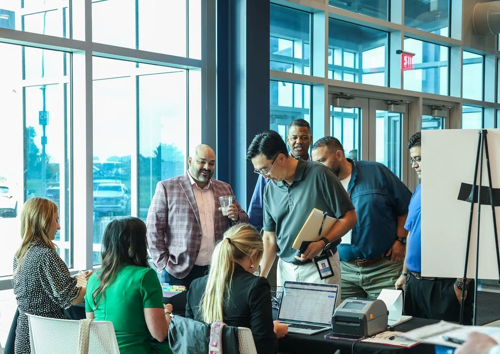 A group of people in a conference room with large windows, engaging and discussing around a table with laptops and papers.