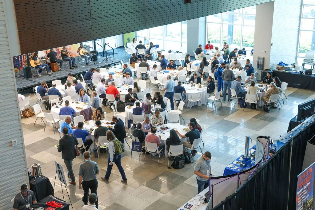 Conference or networking event with round tables, a stage with musicians, and attendees engaging in conversations.