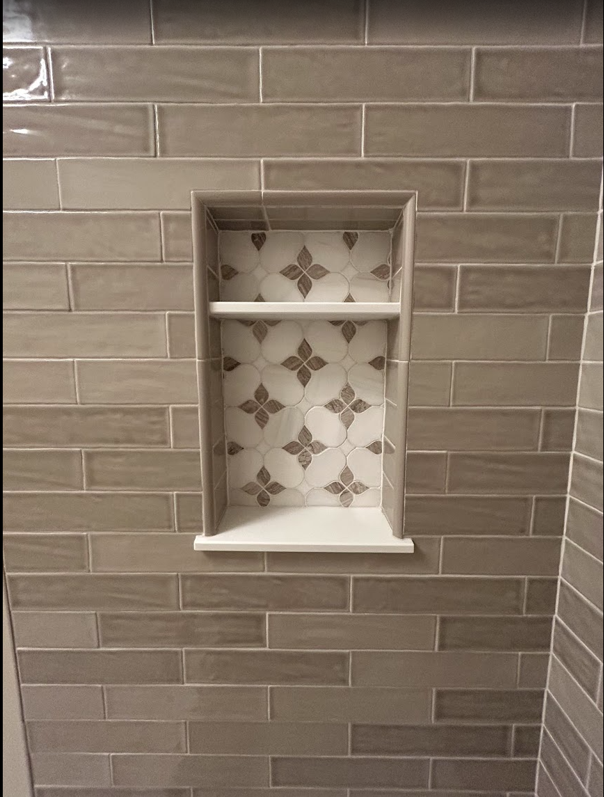 Decorative shower niche detail in a Raleigh, NC taupe guest bath featuring glossy rectangular wall tile, accent tile backing, and clean shelf detail by Parker’s Precision Tile.