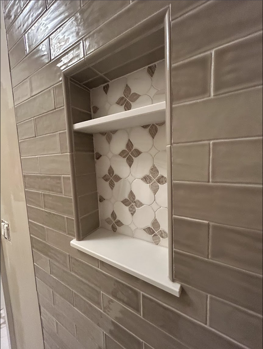 Custom shower niche in a Raleigh, NC guest bathroom with taupe glossy wall tile, decorative accent tile, white shelf detail, and precise tile layout by Parker’s Precision Tile.