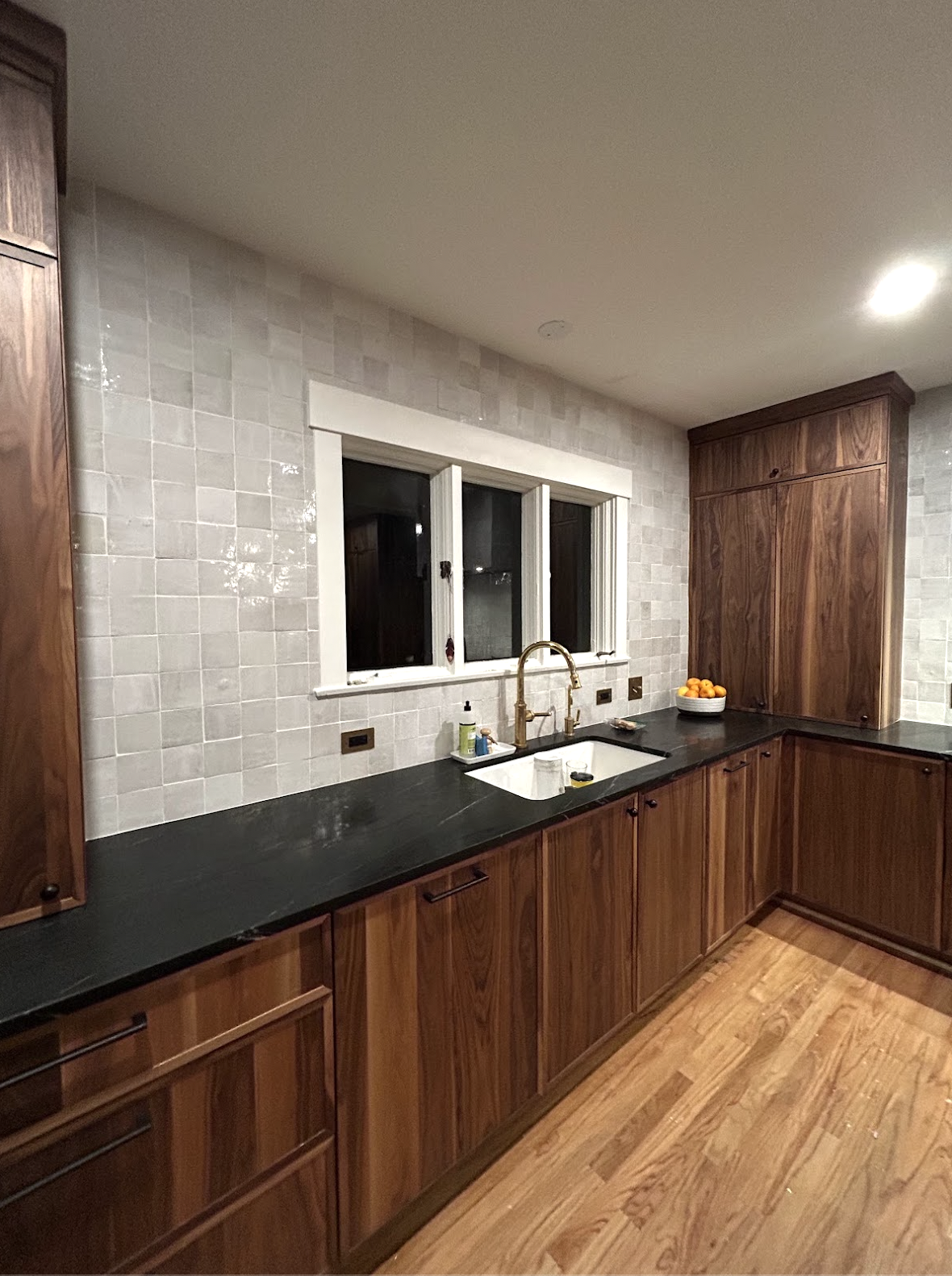 Glossy Zellige kitchen backsplash in Durham, NC installed around a sink wall and window with warm wood cabinetry, dark countertops, and custom tile craftsmanship by Parker’s Precision Tile.
