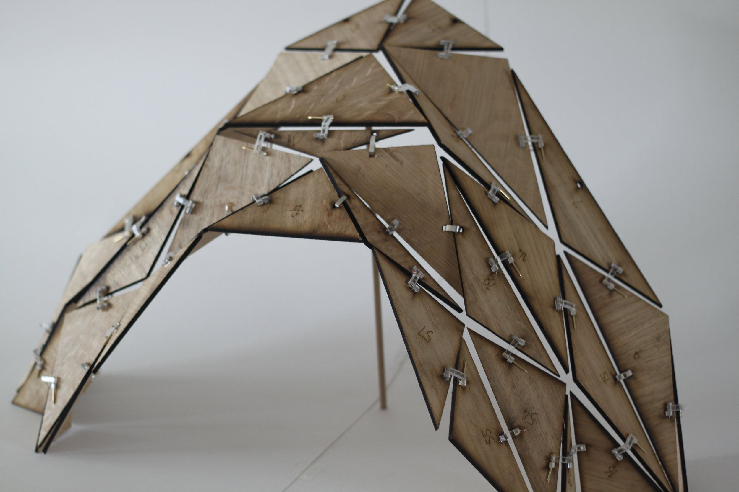 A wooden and metal bird sculpture with geometric shapes, supported by thin metal rods.