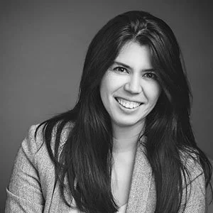 Black and white portrait of a woman with long dark hair, smiling, wearing a light-colored blazer.