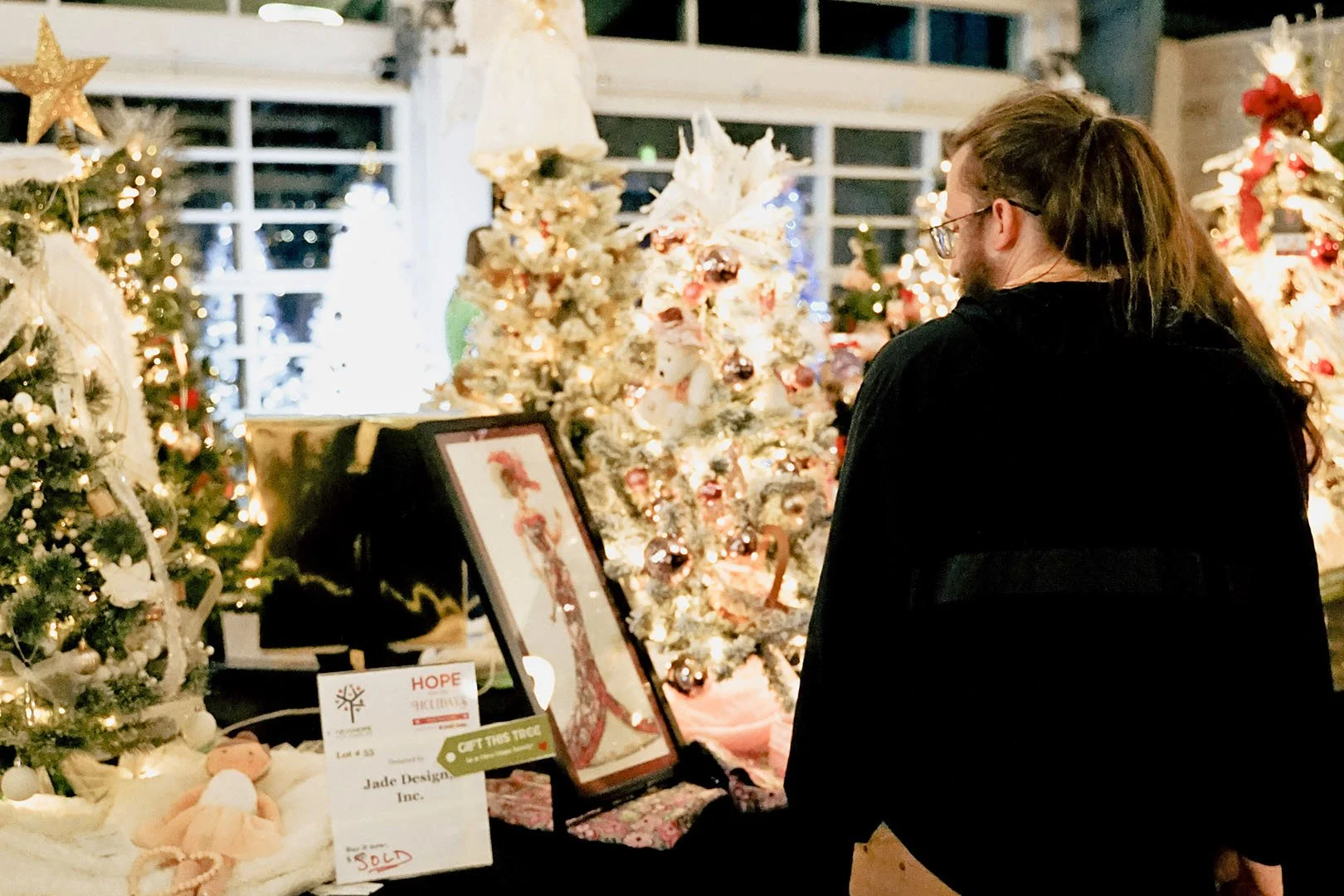 A woman shopping for Christmas decorations in a store filled with decorated Christmas trees and holiday ornaments.