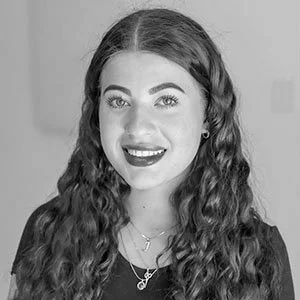 A young woman with curly hair and makeup, smiling at the camera.