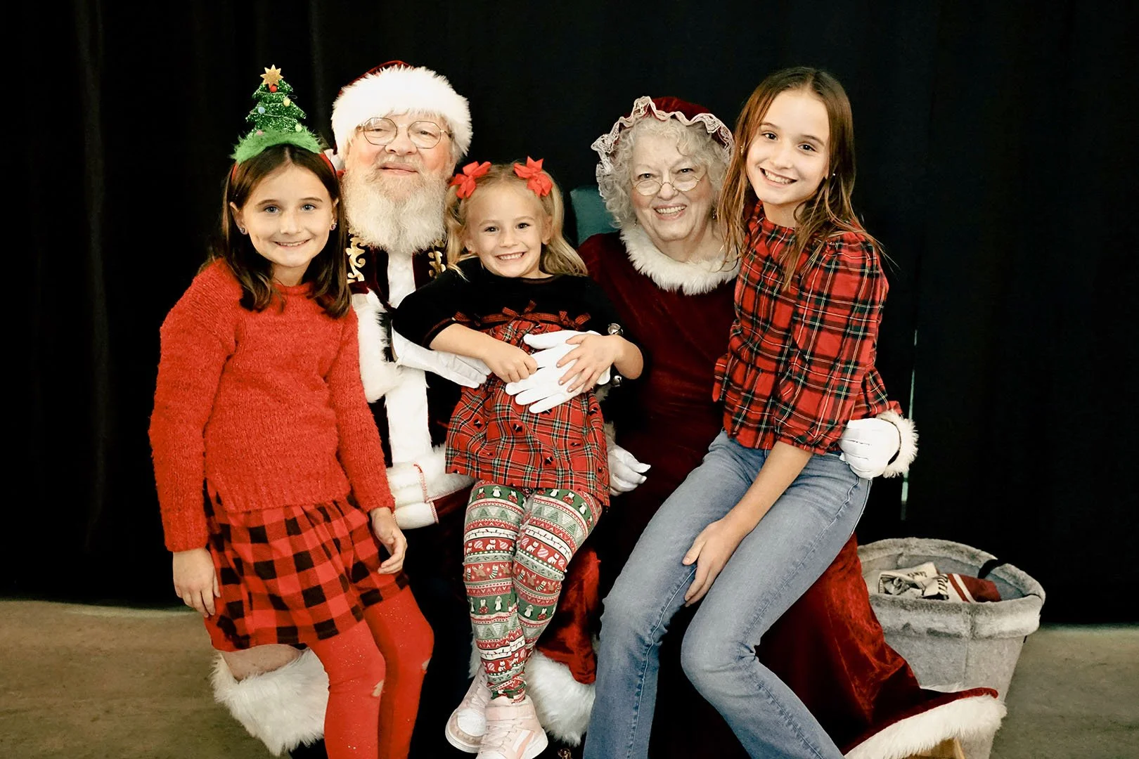 Family photo with children, Santa Claus, and Mrs. Claus during Christmas, all wearing festive attire.