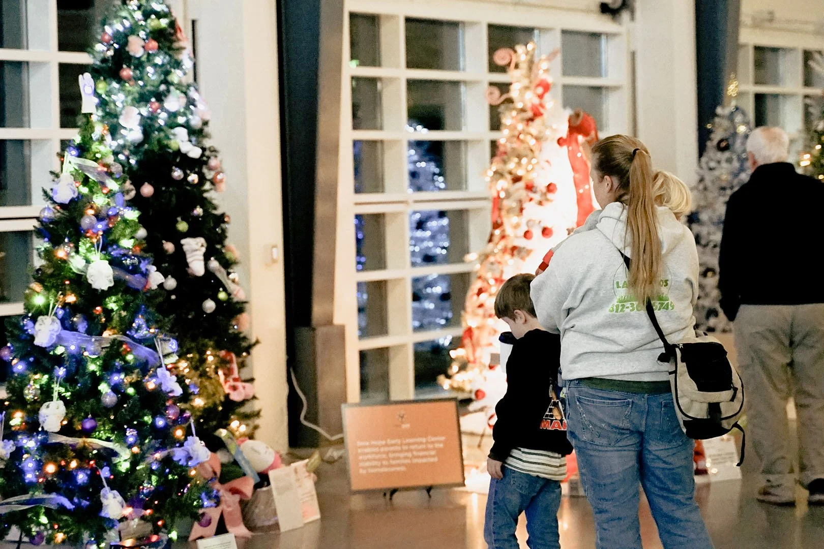 People looking at decorated Christmas trees in an indoor display.