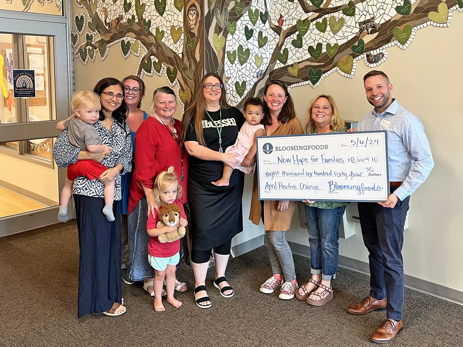 New Hope for Families staff and ELC students at New Hope for Families stand with a ceremonial check from Bloomingfoods