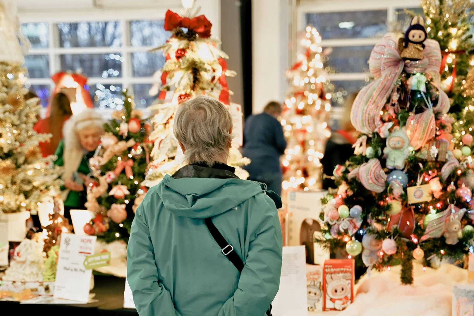 Person in green jacket shopping for Christmas decorated trees in a store