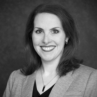 Black-and-white portrait of a woman smiling, wearing a blazer and a necklace.
