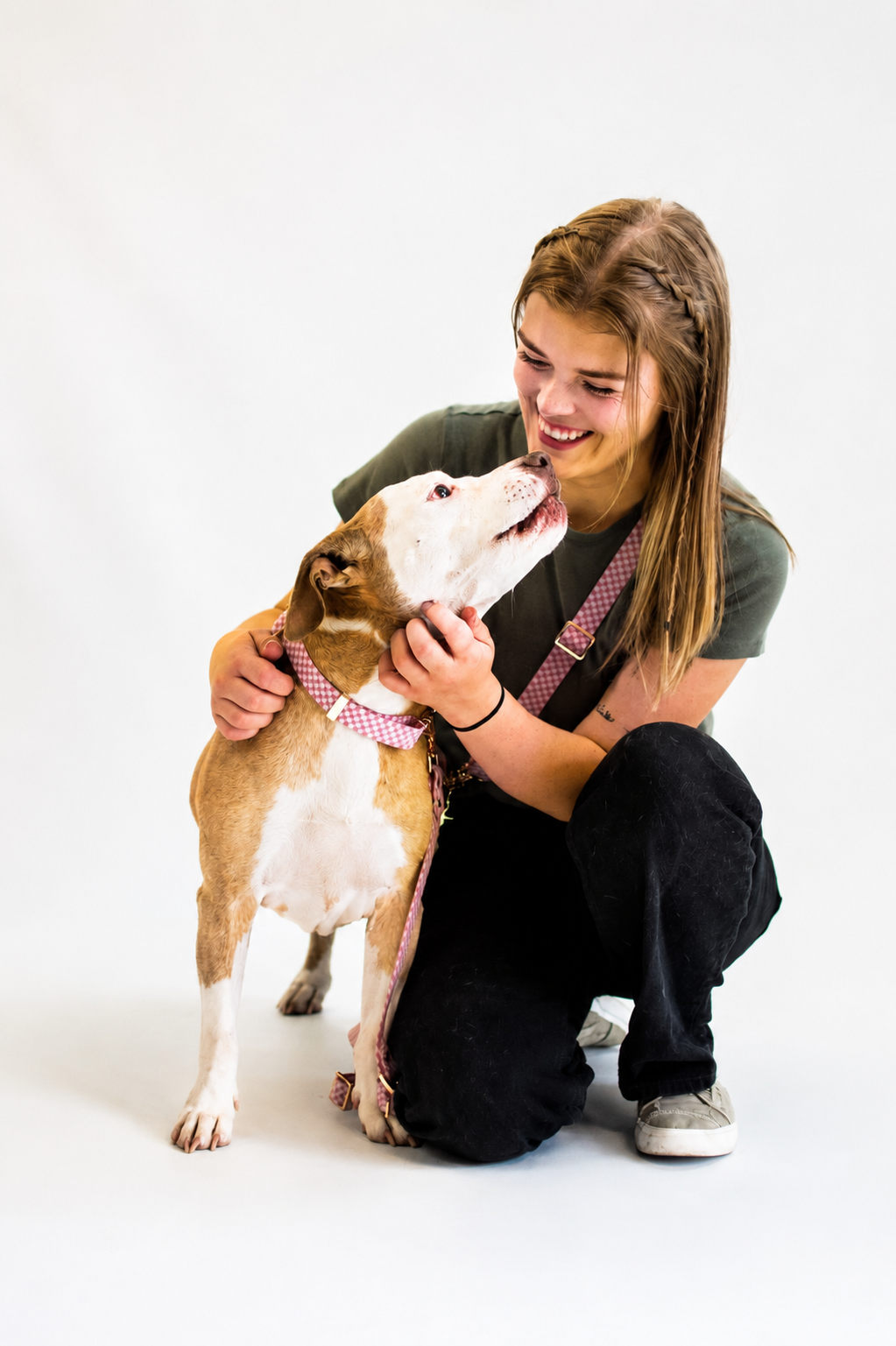 Girl with long hair smiling and petting a brown and white dog against a white background.