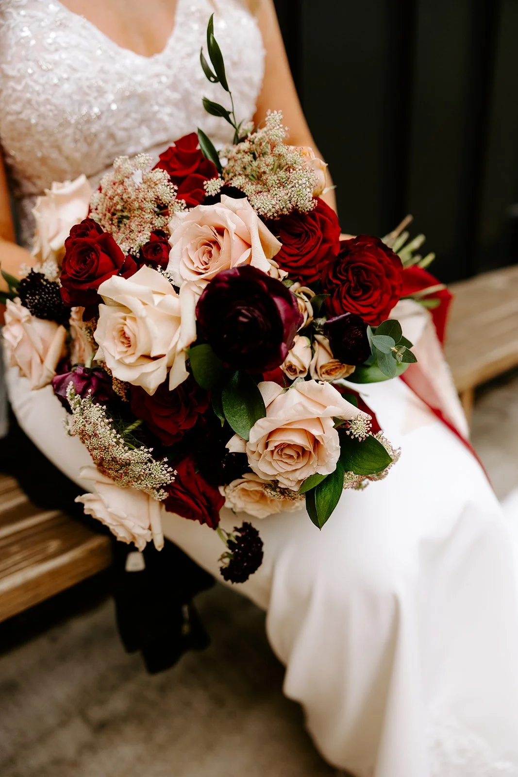 A bride in a wedding dress holding a bouquet of assorted roses, peonies, and greenery.